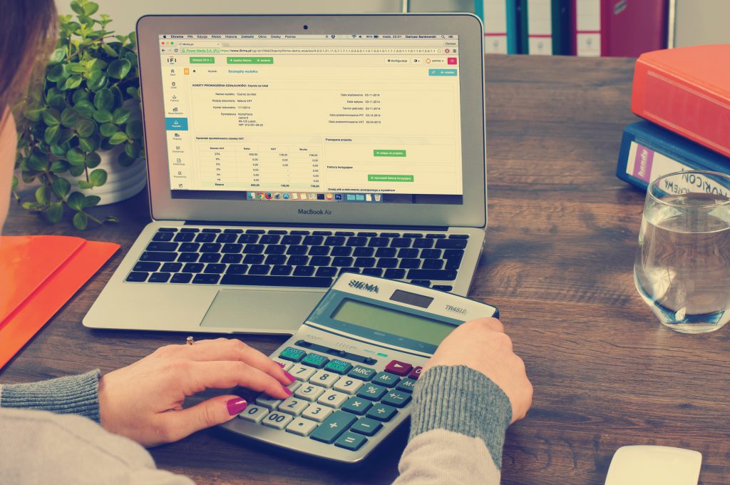 Photographie d'une femme devant un ordinateur affichant une interface de tableur, les mains posées sur sa calculatrice, symbolisant les réglages liés à la TVA pour un site e-commerce.